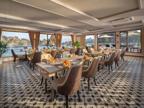 An indoor restaurant with tables set with napkins and glasses, a patterned tile floor, curtains and large windows onto the bay.