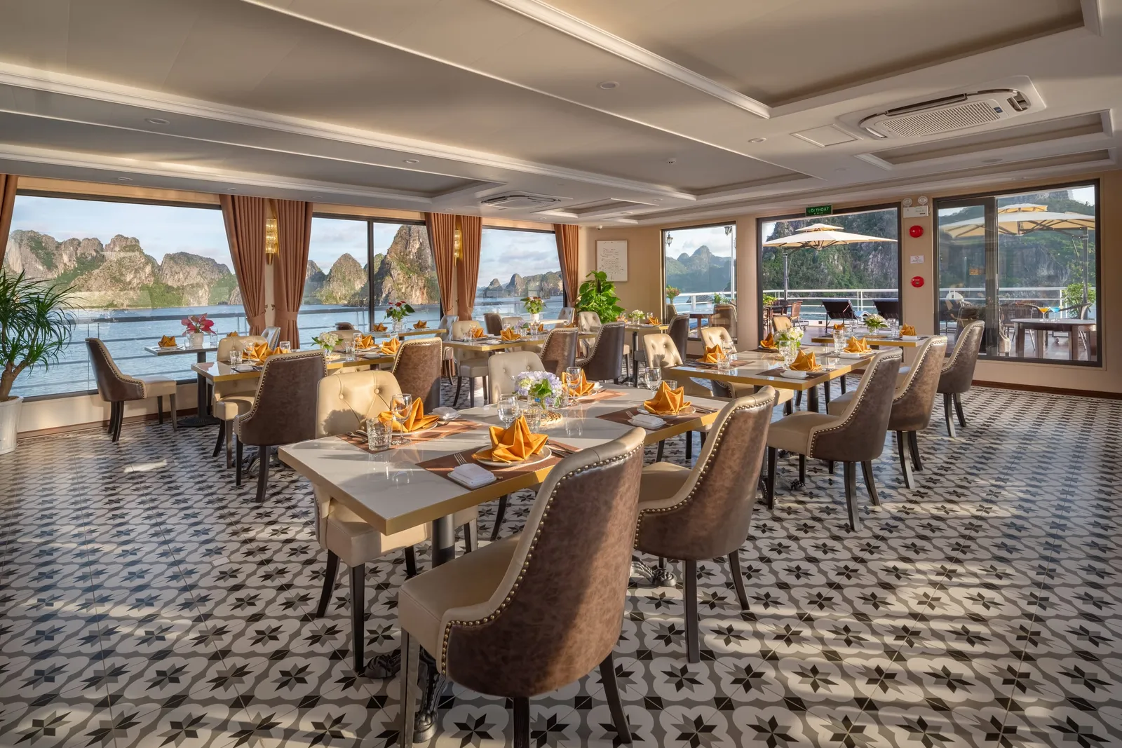An indoor restaurant with tables set with napkins and glasses, a patterned tile floor, curtains and large windows onto the bay.