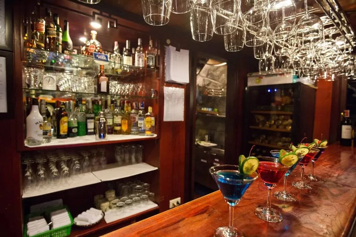 A bar with shelves of bottles and a row of colourful cocktails on the counter.