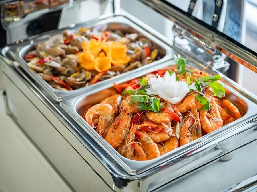 Chafing dishes of stir-fried clams and prawns garnished with carved carrot flowers.