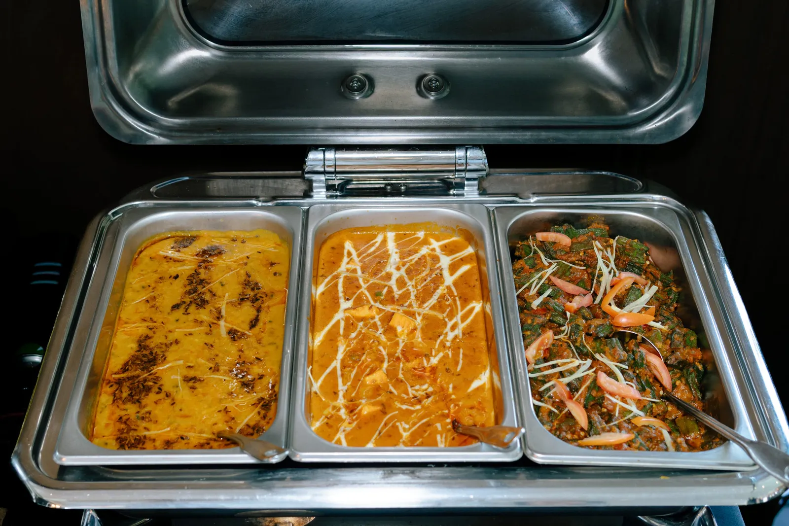 Three metal trays of prepared dishes in a buffet chafing dish with an open lid.