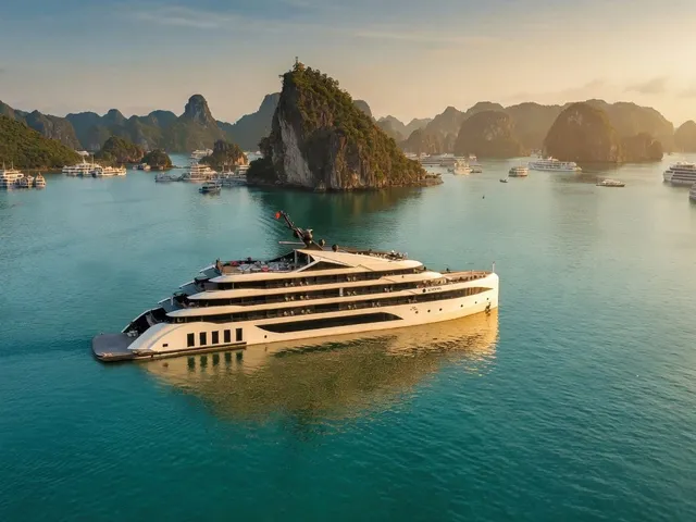 An aerial view at golden hour of a large white multi-deck cruise vessel on turquoise water, with limestone karst islands and many other cruise boats in the background.