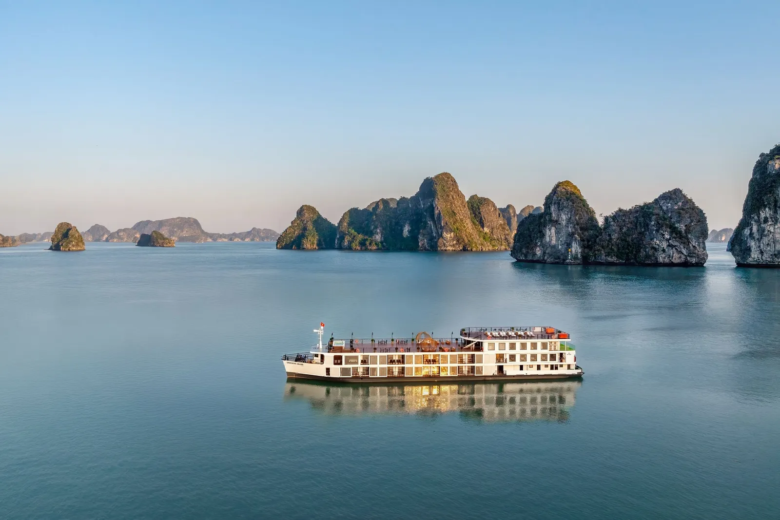 A white multi-deck cruise ship floats on calm water with distinctive limestone karst islands in the background.