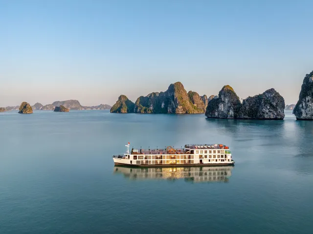 A white multi-deck cruise ship floats on calm water with distinctive limestone karst islands in the background.