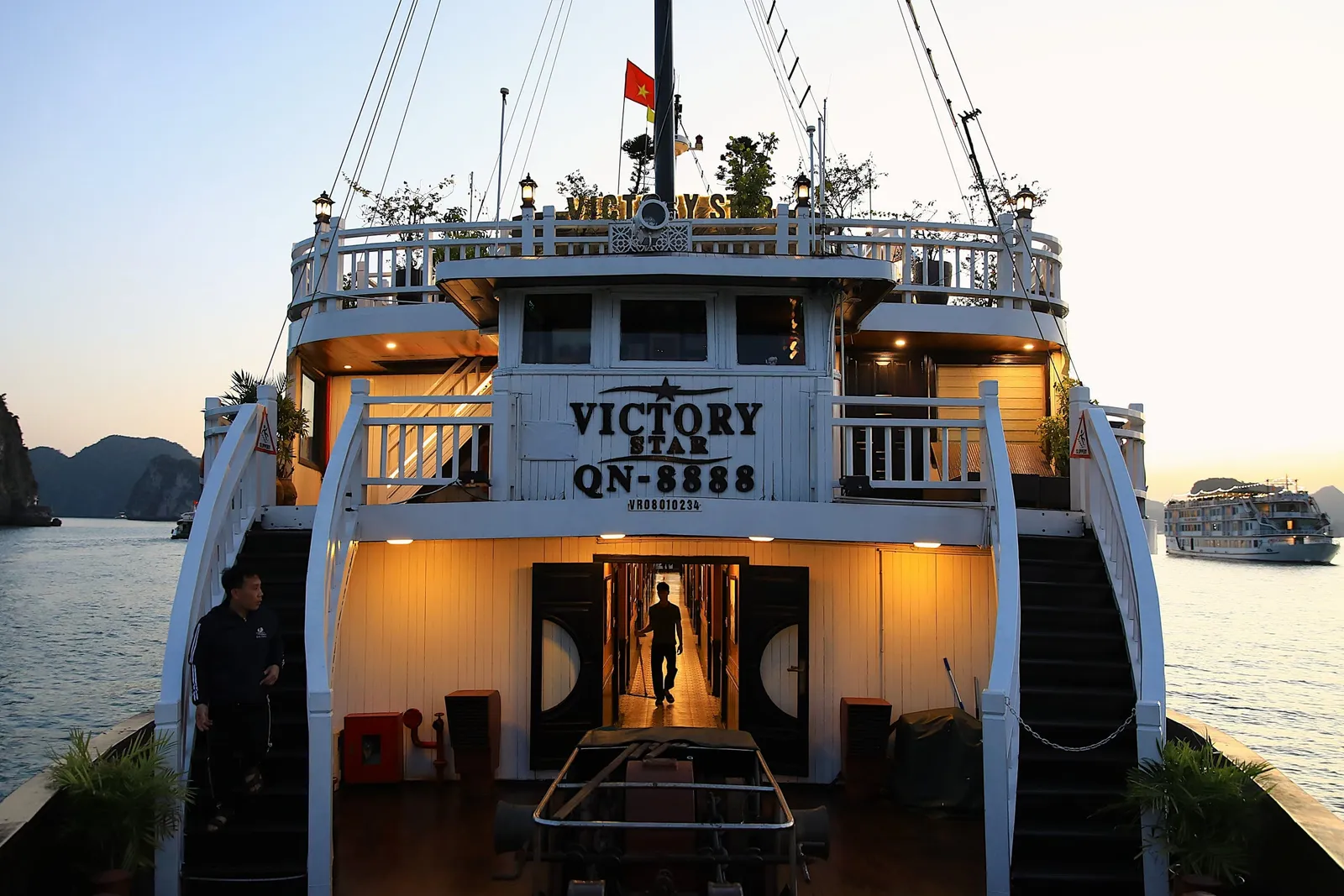 A white cruise boat named Victory Star QN-8888 docked at sunset with limestone karsts visible in the background and another boat in the distance.