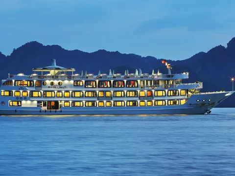 A multi-deck white cruise ship with lit amber windows and the name 'Star Light' on its side sails on calm blue water at dusk in front of dark limestone karst hills, with a Vietnamese flag flying at the top.