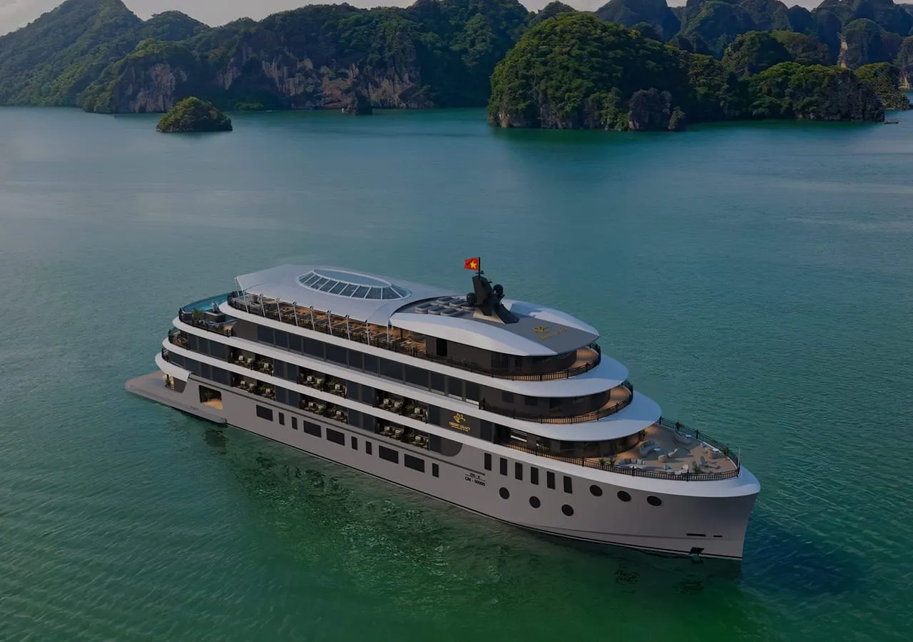 An aerial view of a large multi-deck white cruise ship with a Vietnamese flag on calm green water, with forested limestone karst islands in the background and a small logo emblem on the vessel's side.