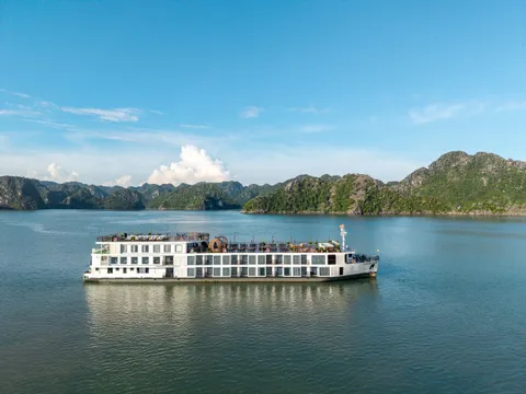 A white multi-deck cruise ship on calm water with limestone karst mountains in the background under blue sky.