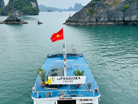 A blue and white cruise boat with Vietnamese flag and Le Pandora Cruise signage on its upper deck, photographed from above in calm waters surrounded by limestone karst formations.