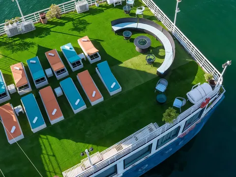 A top-down view of the grass-turf sundeck with orange and teal loungers, with the blue hull edge and a sail visible.