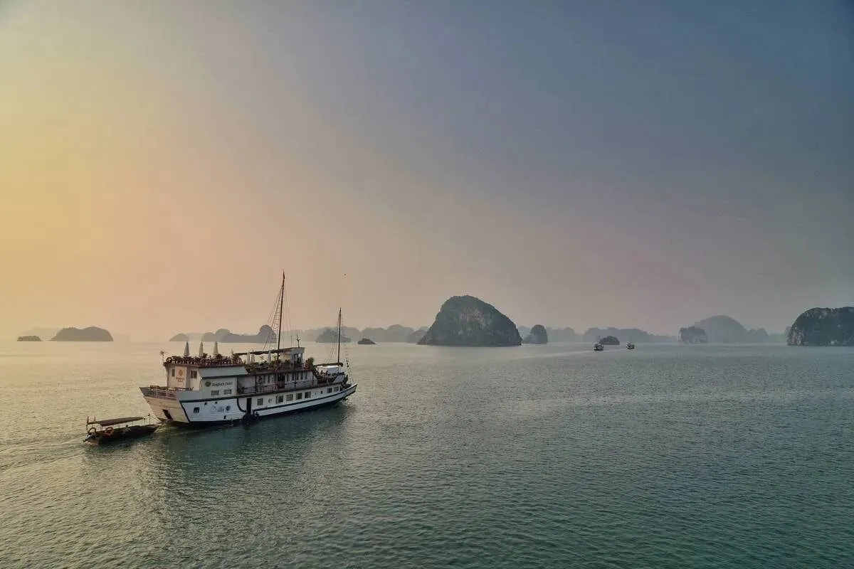 A wooden cruise junk in misty morning light, moving across the bay past small karst islands.