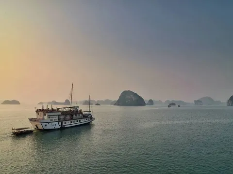 A wooden cruise junk in misty morning light, moving across the bay past small karst islands.