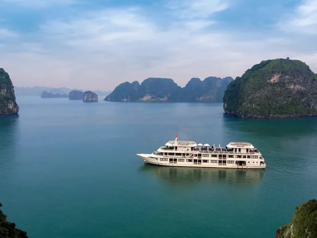 A white multi-deck cruise ship floats in calm turquoise water surrounded by dramatic limestone karst islands.