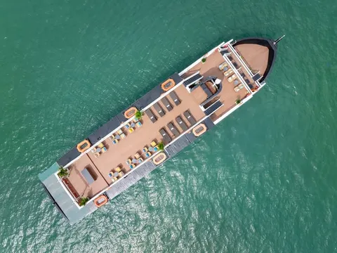 Top-down aerial view of a cruise boat on turquoise water, showing the wooden sundeck with rows of loungers.