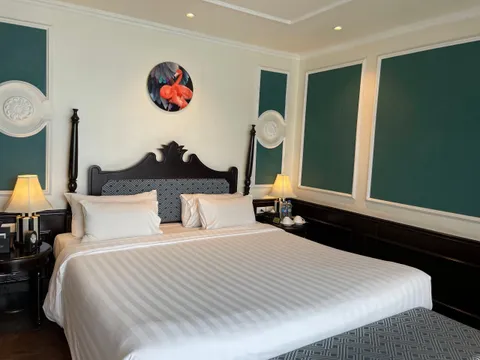 A cabin with a large white-linen bed, dark wood headboard and posts, two lit bedside lamps, teal wall panels with white molding, and a round flamingo artwork above the bed.