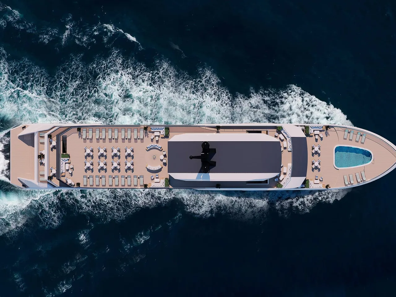 A top-down aerial view of a large cruise vessel with a sun deck, lounge chairs, tables and a small pool at the bow, moving through dark blue open water with a white wake behind it.