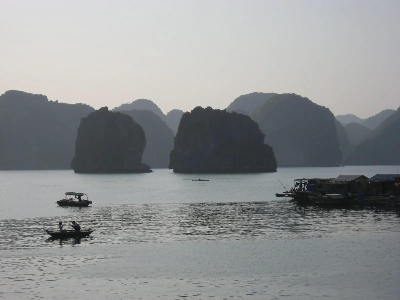 Limestone islands over calm water, with small boats in the foreground