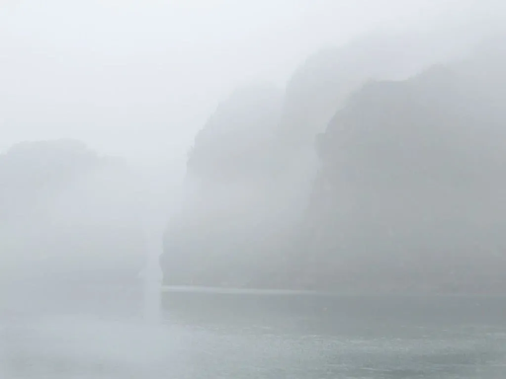 Limestone islands almost hidden in thick fog over grey water