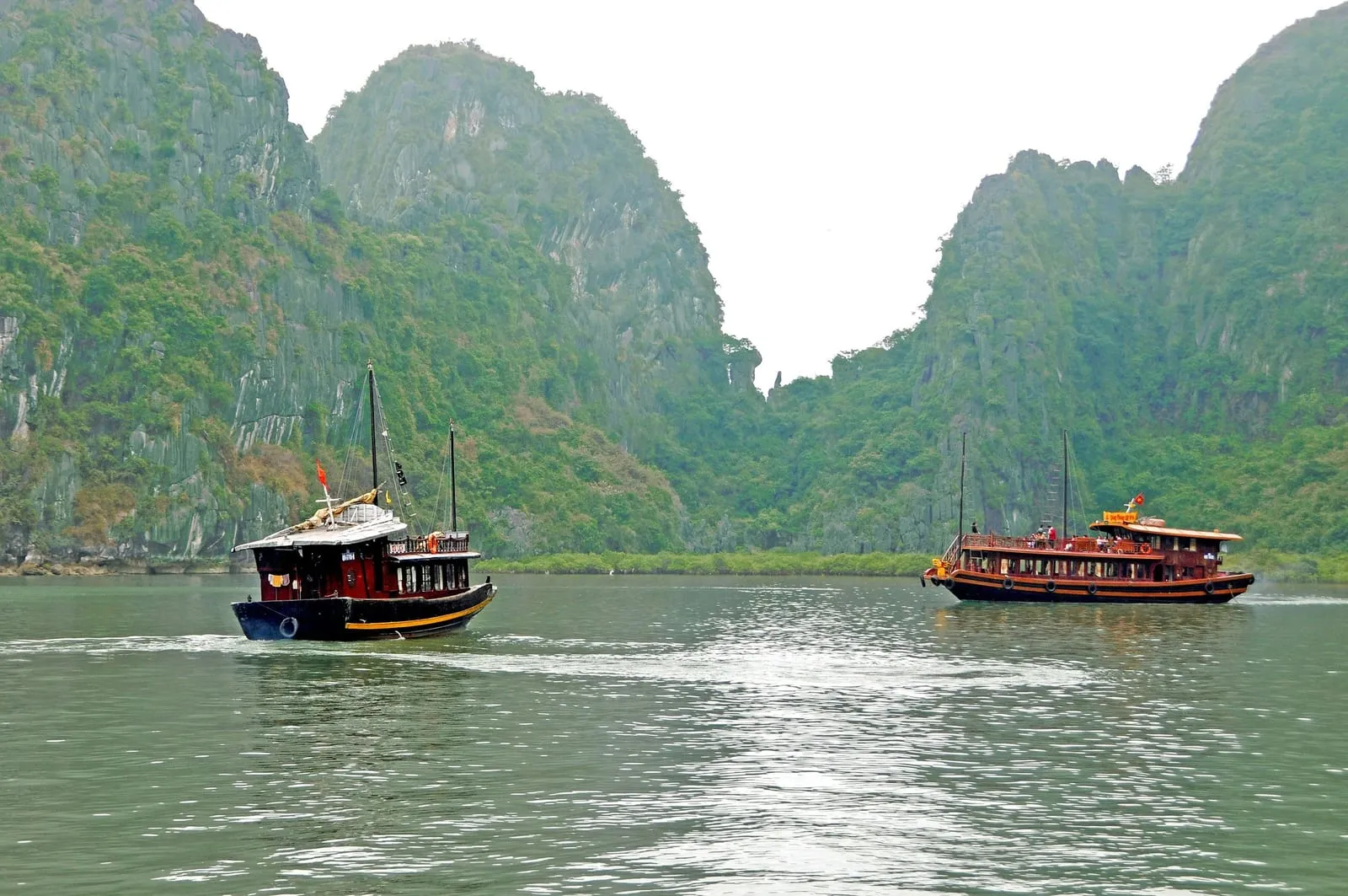 Two wooden tour boats crossing open water in front of limestone hills