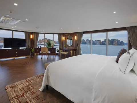 Suite bedroom with a herringbone timber floor, a wide bed and floor-to-ceiling windows wrapping round to karst views