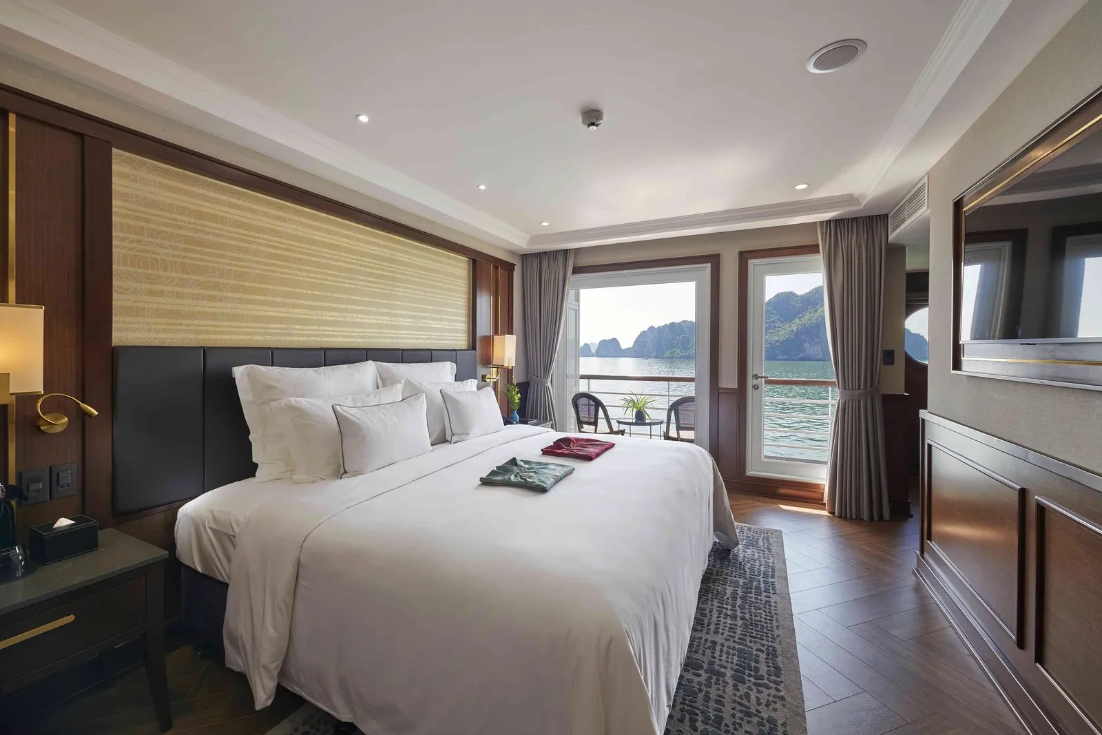 Deluxe balcony cabin with a woven headboard panel, white bed and glass doors onto a balcony over the bay