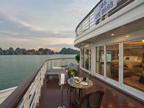 Wraparound suite terrace at the bow with loungers and a small table, the registration QN-9698 on the deck above, karst at dusk