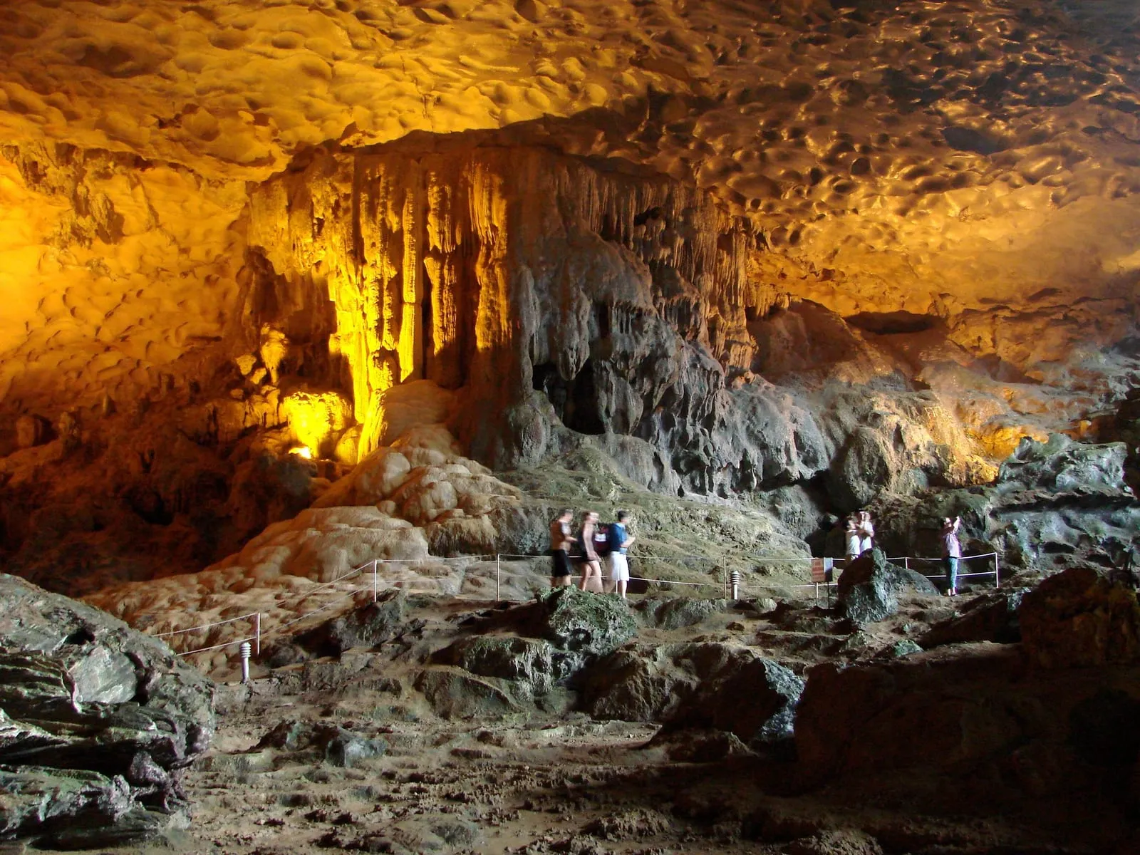 Visitors on the path through a lit chamber of Sung Sot Cave, with rock formations overhead