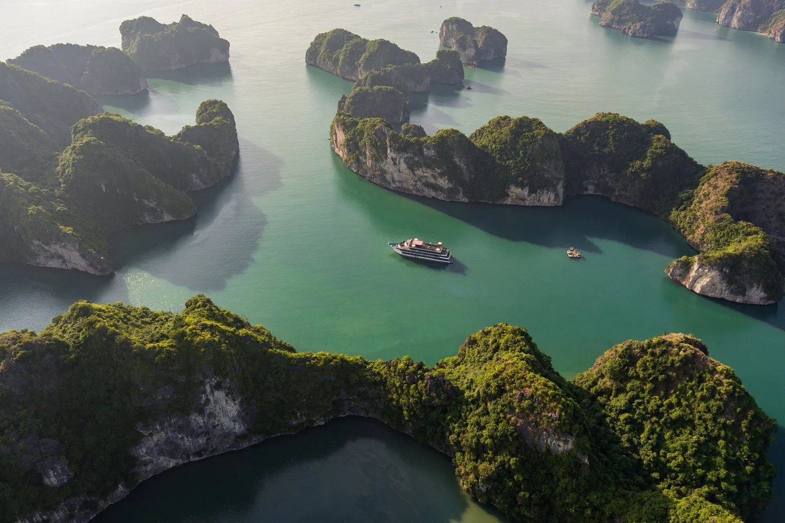 Aerial view of green limestone karst islands in calm turquoise water with a single cruise ship and a small boat in the middle.