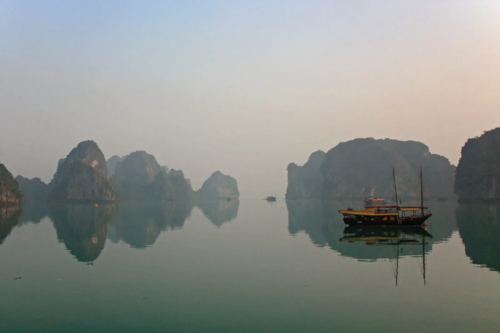 A wooden boat on still water among limestone islands at sunrise