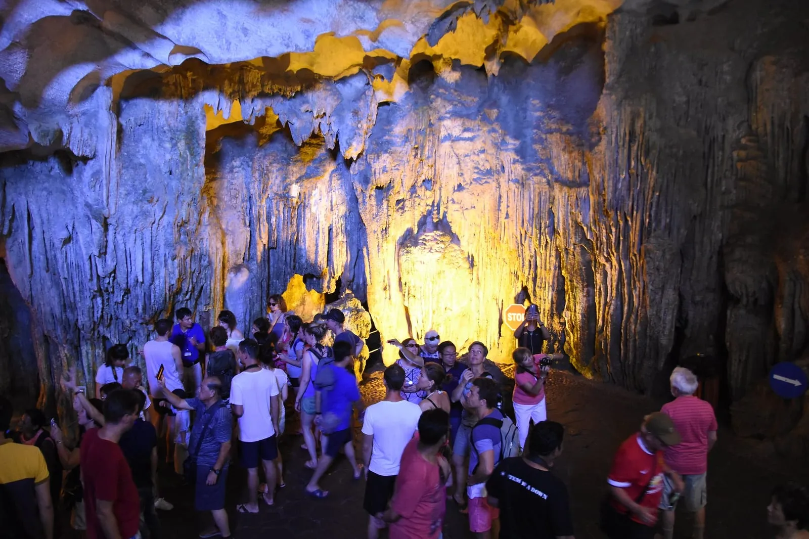 A dense crowd of visitors inside a lit cave chamber in Ha Long Bay