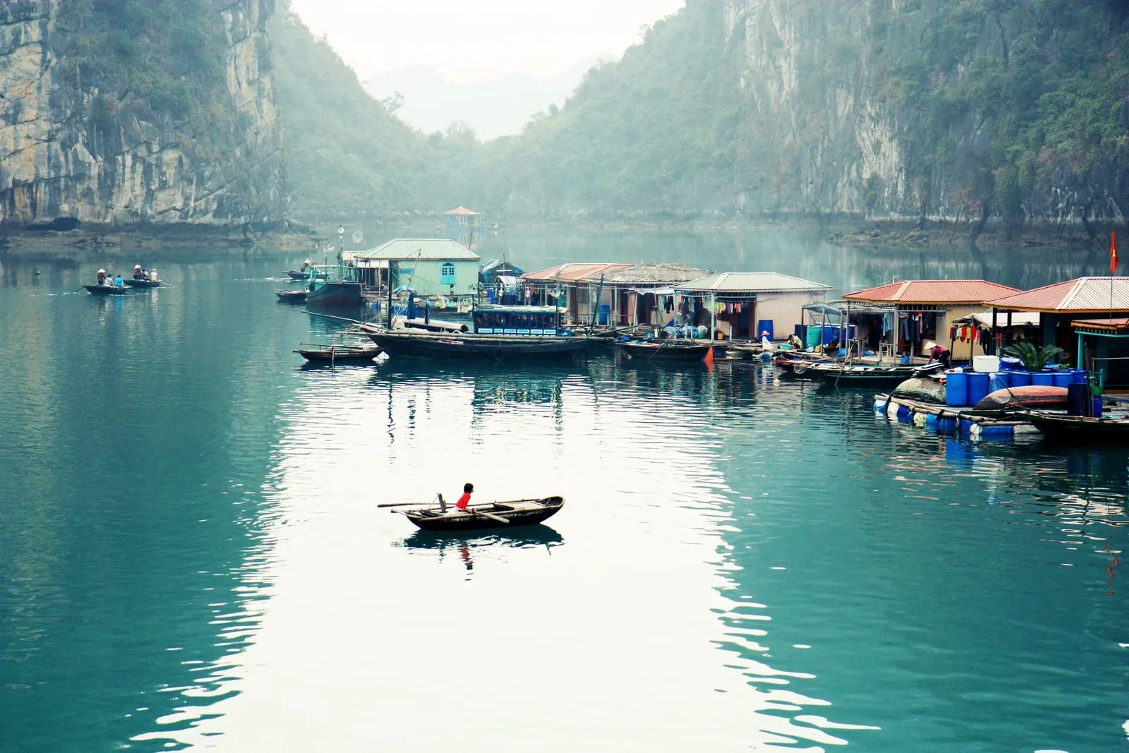 Floating houses and a small rowing boat in a channel between limestone cliffs